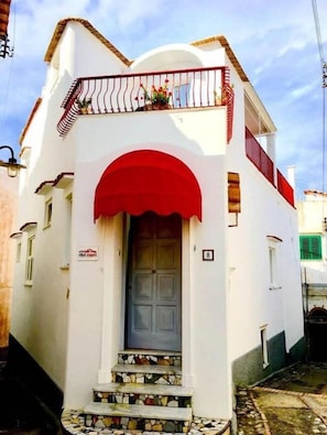 A white building with a red awning, a balcony with a railing, and a door with a small window above it. - R&D Rest and Dream Capri (Anacapri)