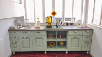 A kitchen with a green cabinet, a coffee maker, a kettle, and a window with a view.
