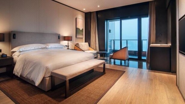 A modern hotel room with a large bed, a bench, a desk, and a view of the city. - Guangzhou Y&W Service Apartment (Guangzhou)