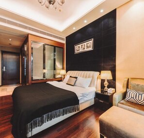 A modern hotel room with a large bed, a sitting area with a sofa, a desk, and a large mirror.