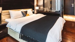 A modern hotel room with a large bed, dark wood paneling, a large mirror, and a door with a glass panel. - Guangzhou Y&W Service Apartment (Guangzhou)