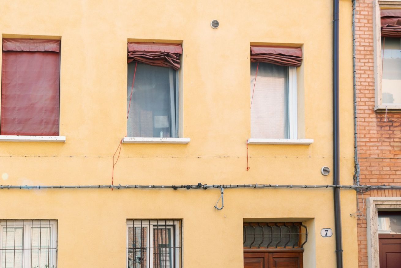Un edificio amarillo con tres ventanas, cada una con cortinas. Se ve el número 7 en el edificio.