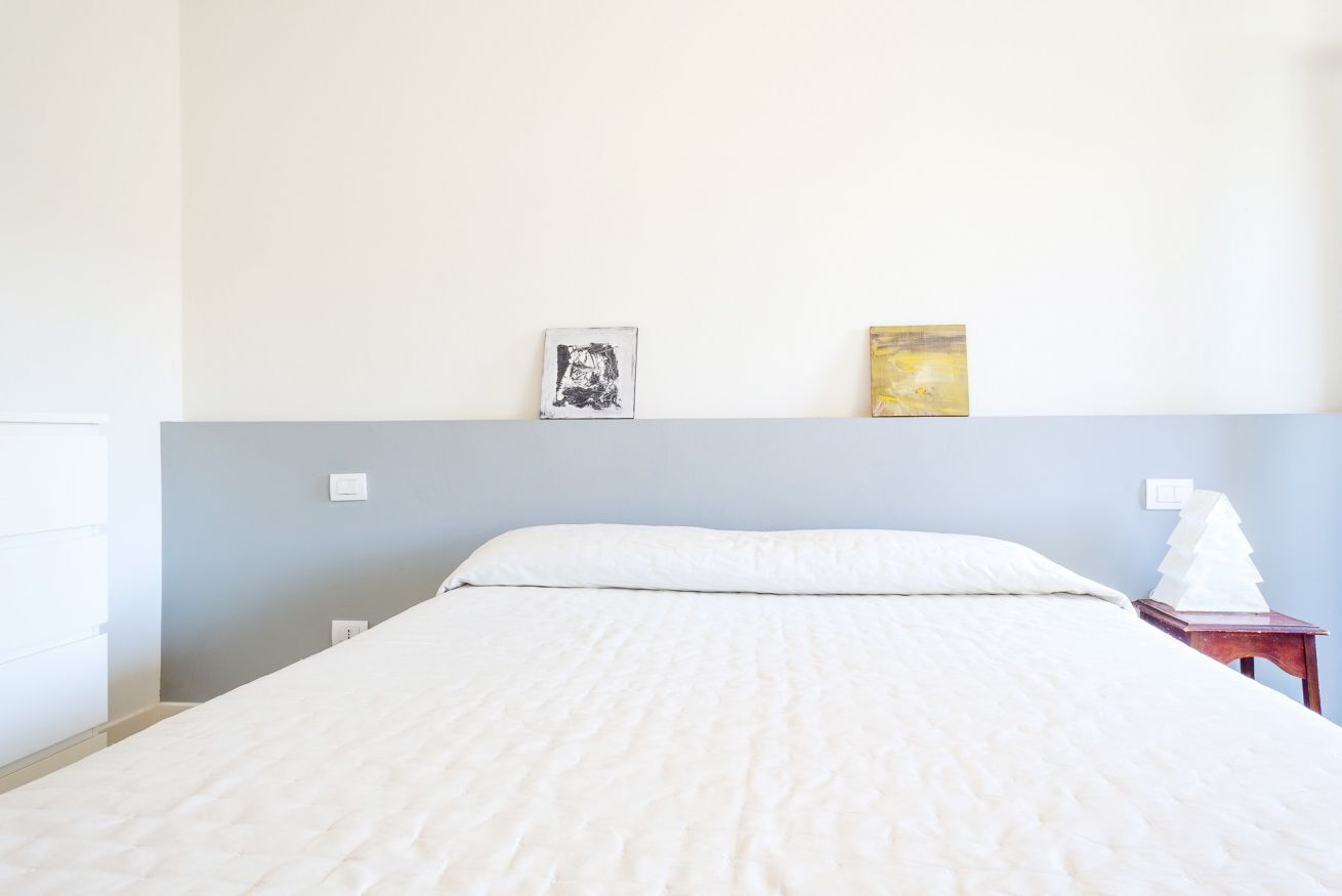 Ein Bett mit weißer Bettdecke, ein Nachttisch mit einer weißen Lampe und zwei Kunstwerke an der Wand.