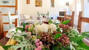 Une table à manger agrémentée d’un centre de table floral, un coin repas avec des chaises, un canapé et un téléviseur en arrière-plan.