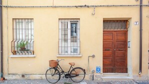 Un vélo est garé devant un bâtiment dont la porte est en bois et dont la fenêtre est munie de barreaux métalliques.