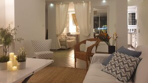 A modern living room with a sofa, two patterned chairs, a dining table with candles, and a view of the city at night through a window.