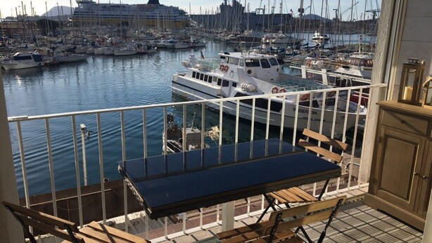 A balcony with a table and chairs overlooking a marina with boats and a cruise ship.