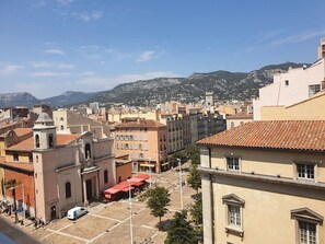 Un paysage urbain avec des bâtiments historiques, une place centrale et une chaîne de montagnes en arrière-plan.