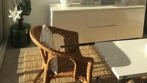 A well-lit room with a dining table, wicker chair, and a cabinet with decorative items.