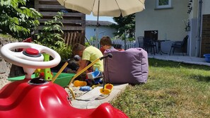 A red toy car with a steering wheel, a purple bag, and a child playing with a toy shovel.