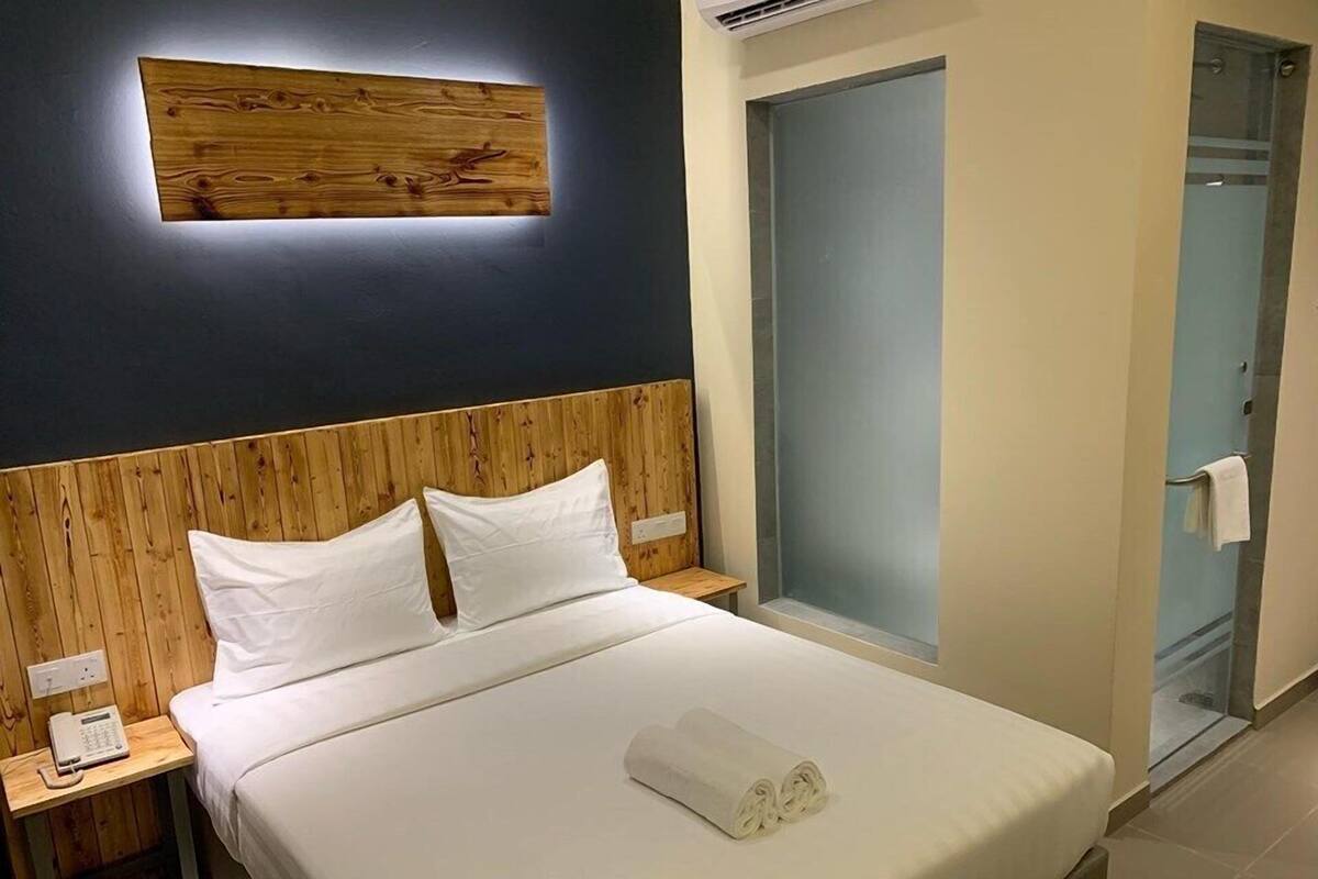 A hotel room with a wooden headboard, a bed with white linens, a bedside phone, and a glass shower door.