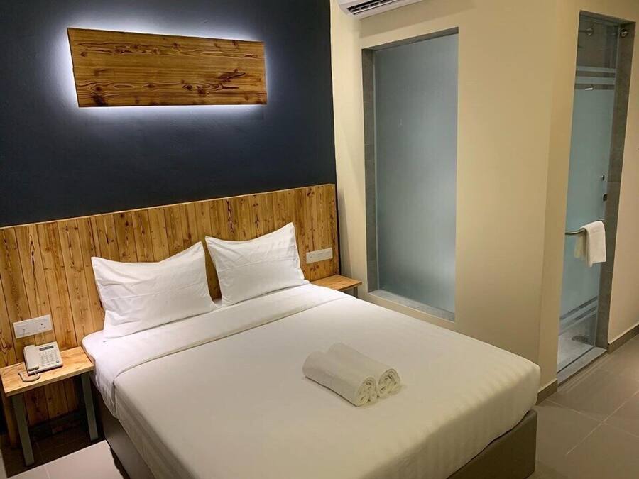 Quarto de hotel com cabeceira de madeira, cama com roupa de cama branca, telefone ao lado da cama e porta de box de vidro.