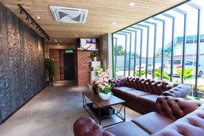 A modern lobby with a leather sofa, a wooden coffee table, and a large window with a view of parked cars. - TLJ Hotel (Pelabuhan Klang)