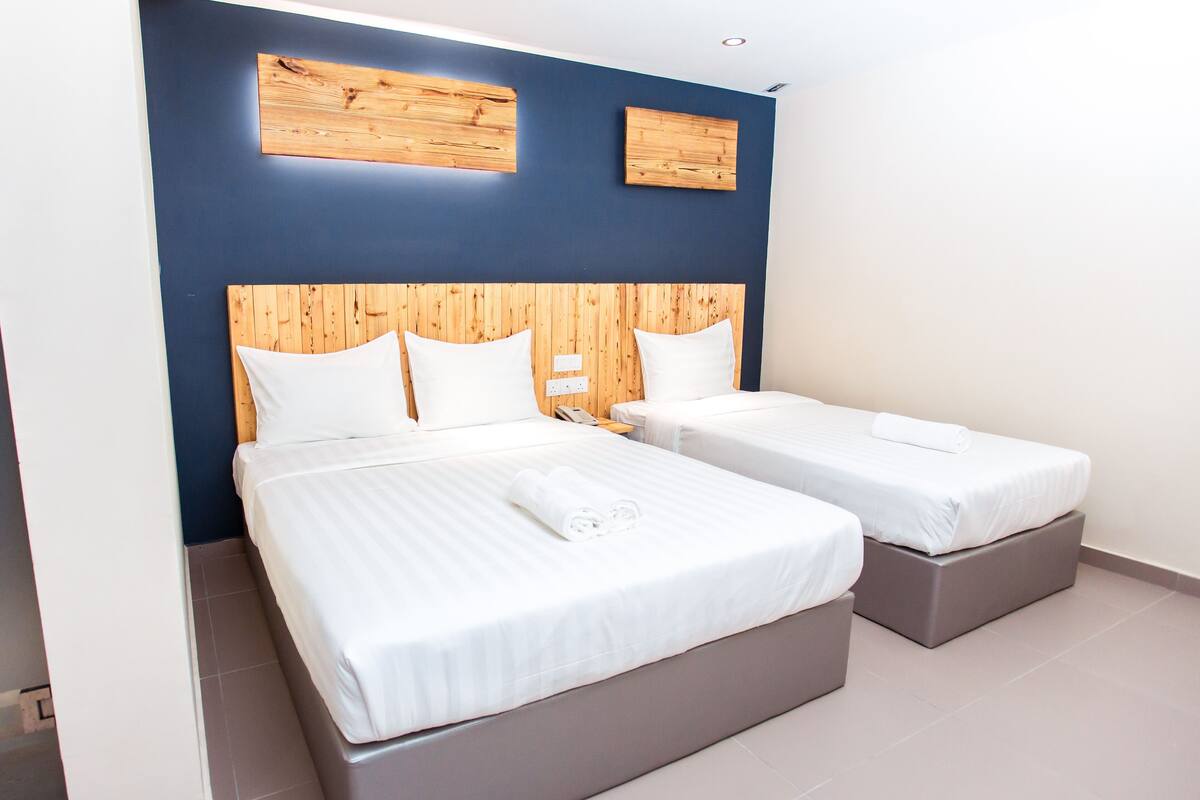 A hotel room with two single beds, wooden headboards, and a blue accent wall.
