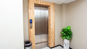 An elevator with a wooden frame, a trash bin, and a potted plant. - TLJ Hotel (Pelabuhan Klang)