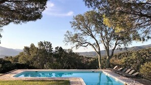 Ein rechteckiger Pool mit Steinrand, umgeben von Gras und Bäumen, mit Blick auf ferne Hügel.