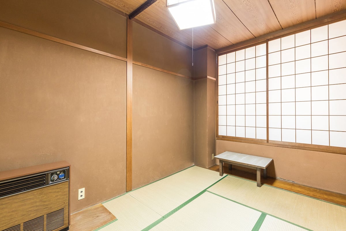 A traditional Japanese room with tatami flooring, a low wooden bench, a heater, and a shoji screen.