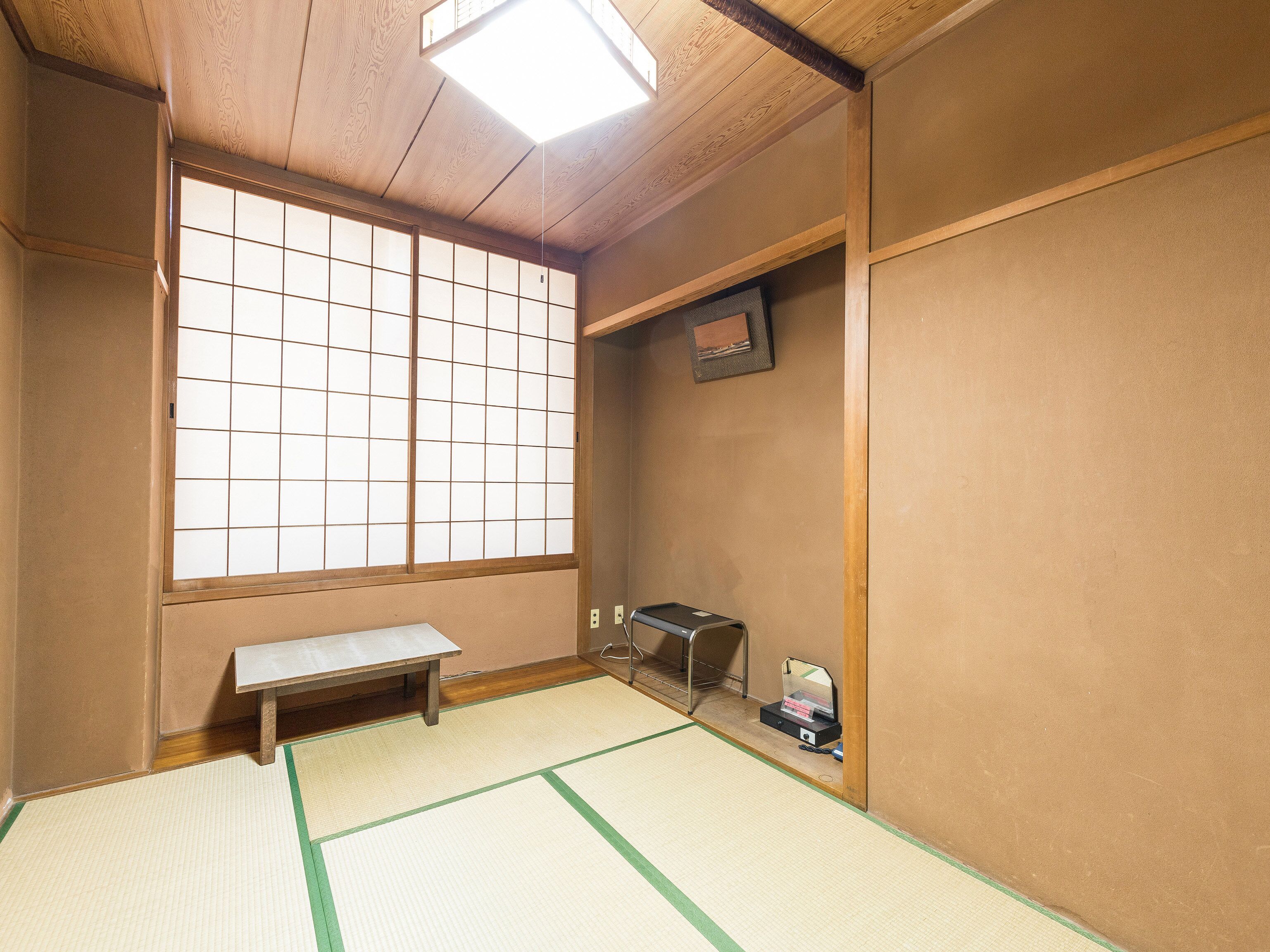 A traditional Japanese room with tatami flooring, a shoji screen window, a small bench, and a desk with a mirror and a small item on it.