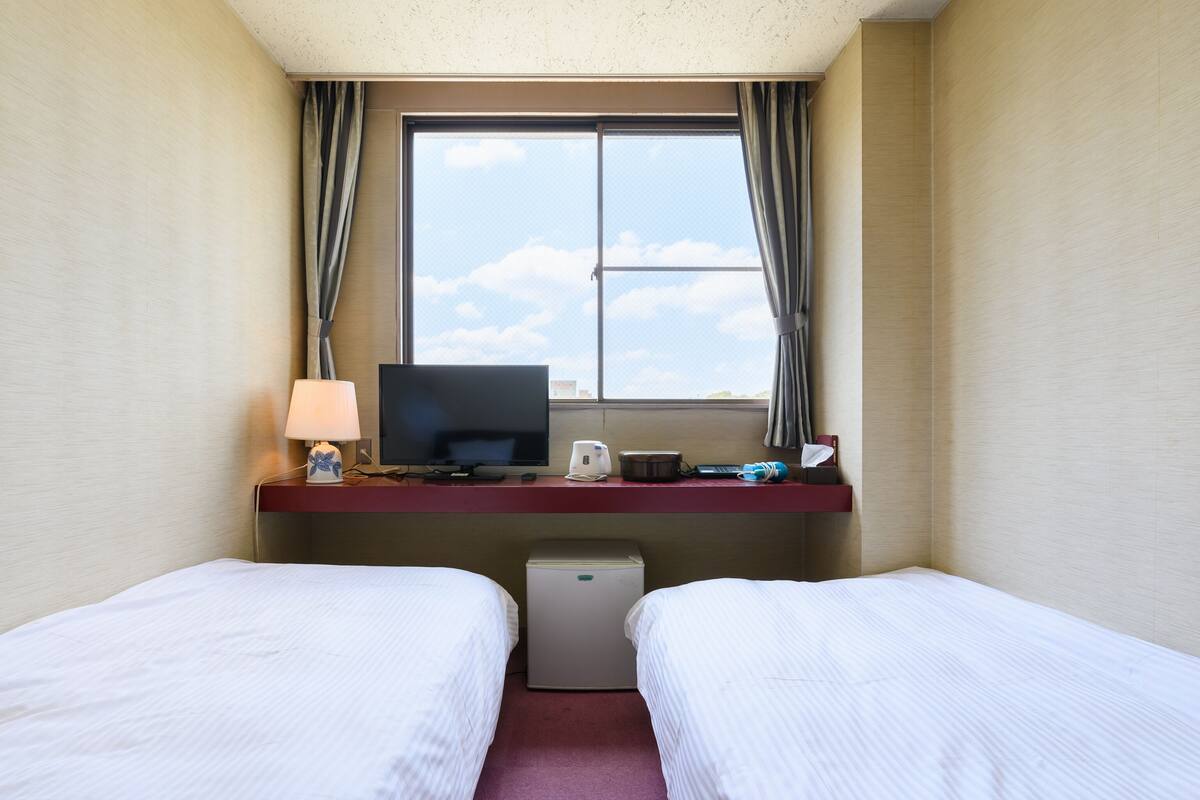 A hotel room with two beds, a desk with a computer, a lamp, and a window with curtains.