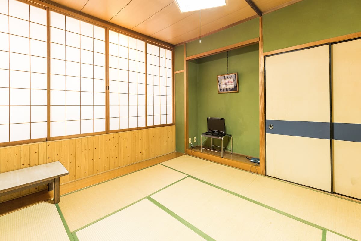 A tatami mat room with a wooden bench, a laptop on a shelf, and a framed picture on the wall.