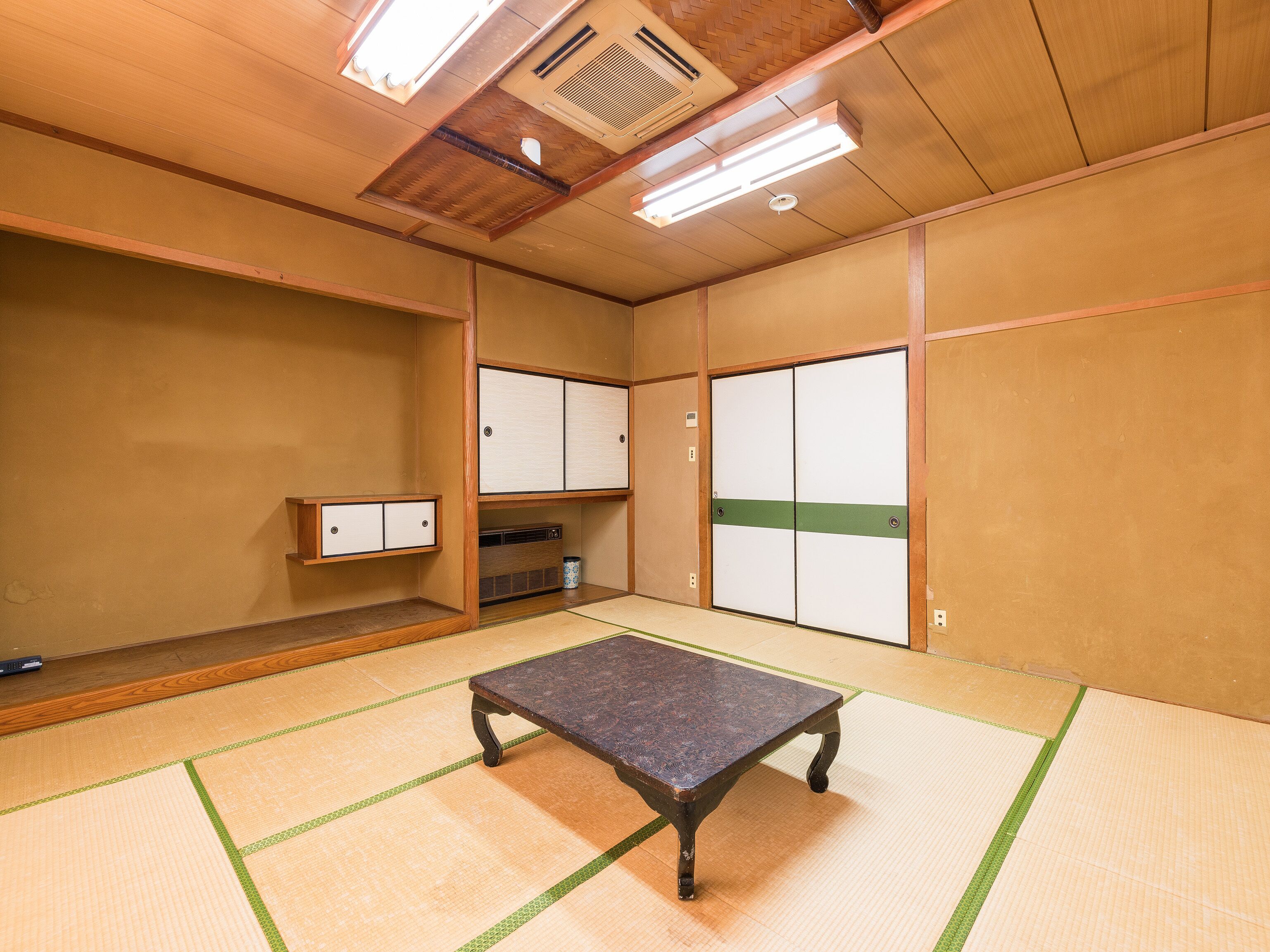 A tatami mat room with a tatami mat table, wooden cabinets, and a ceiling vent.