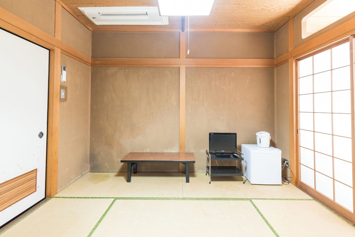 A traditional Japanese room with tatami flooring, a low wooden table, a black TV stand, and a white refrigerator.