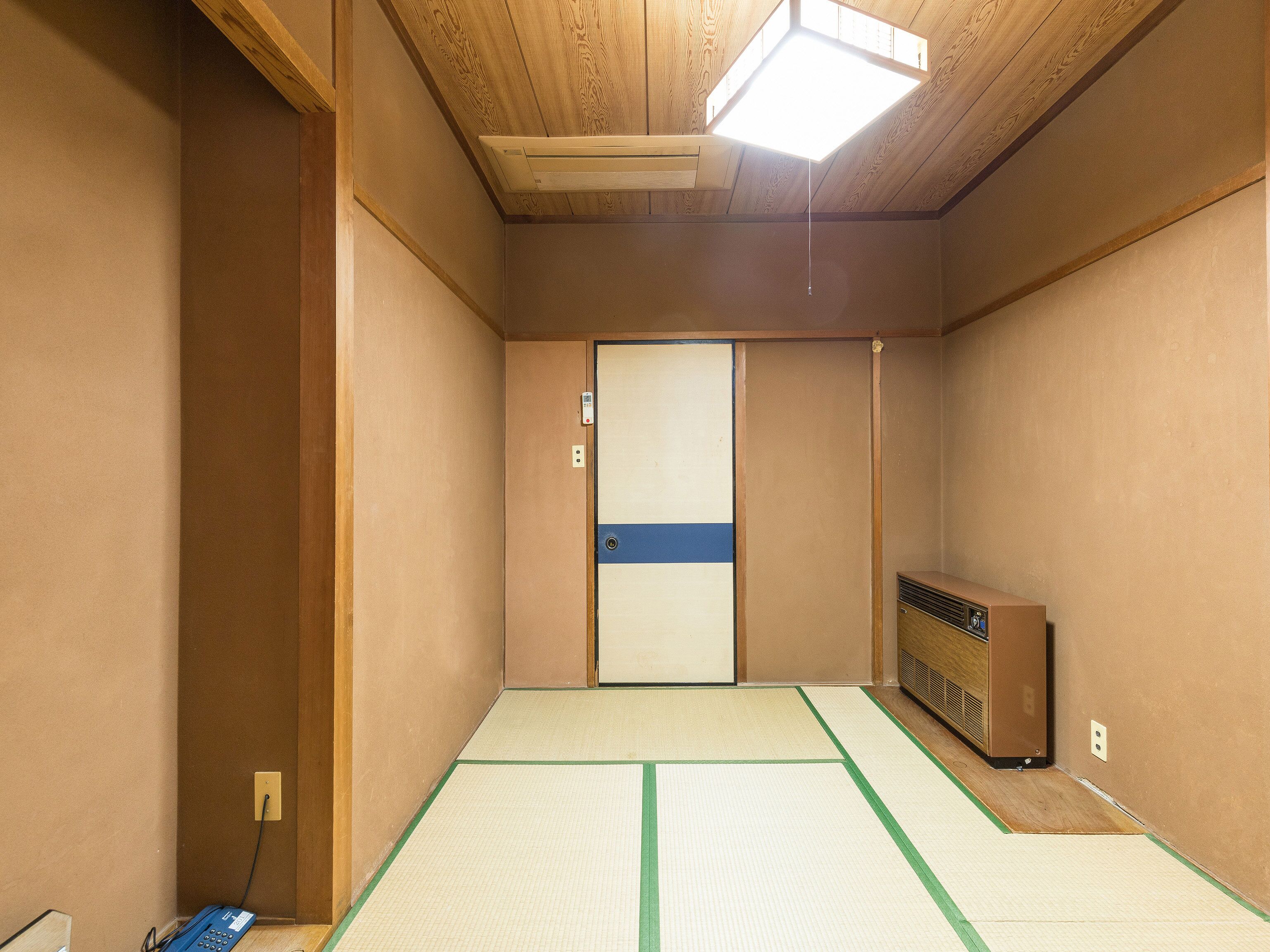 A room with tatami flooring, a sliding door, a heater, and a small table with a blue telephone.