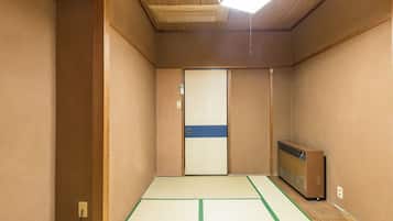 A room with tatami flooring, a sliding door, a heater, and a small table with a blue telephone.