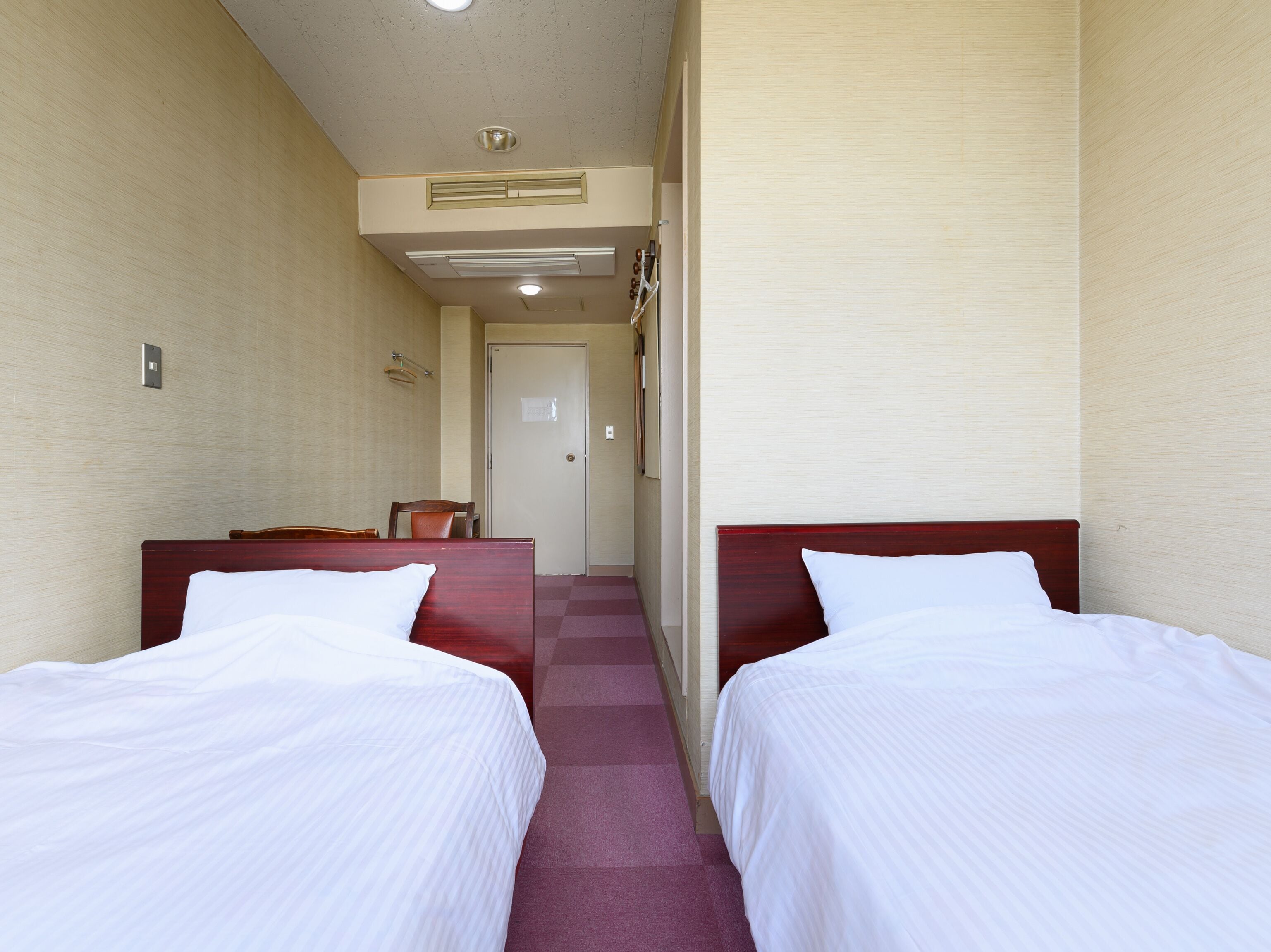 A hotel room with two single beds, a wooden headboard, a checkered floor, and a door in the background.