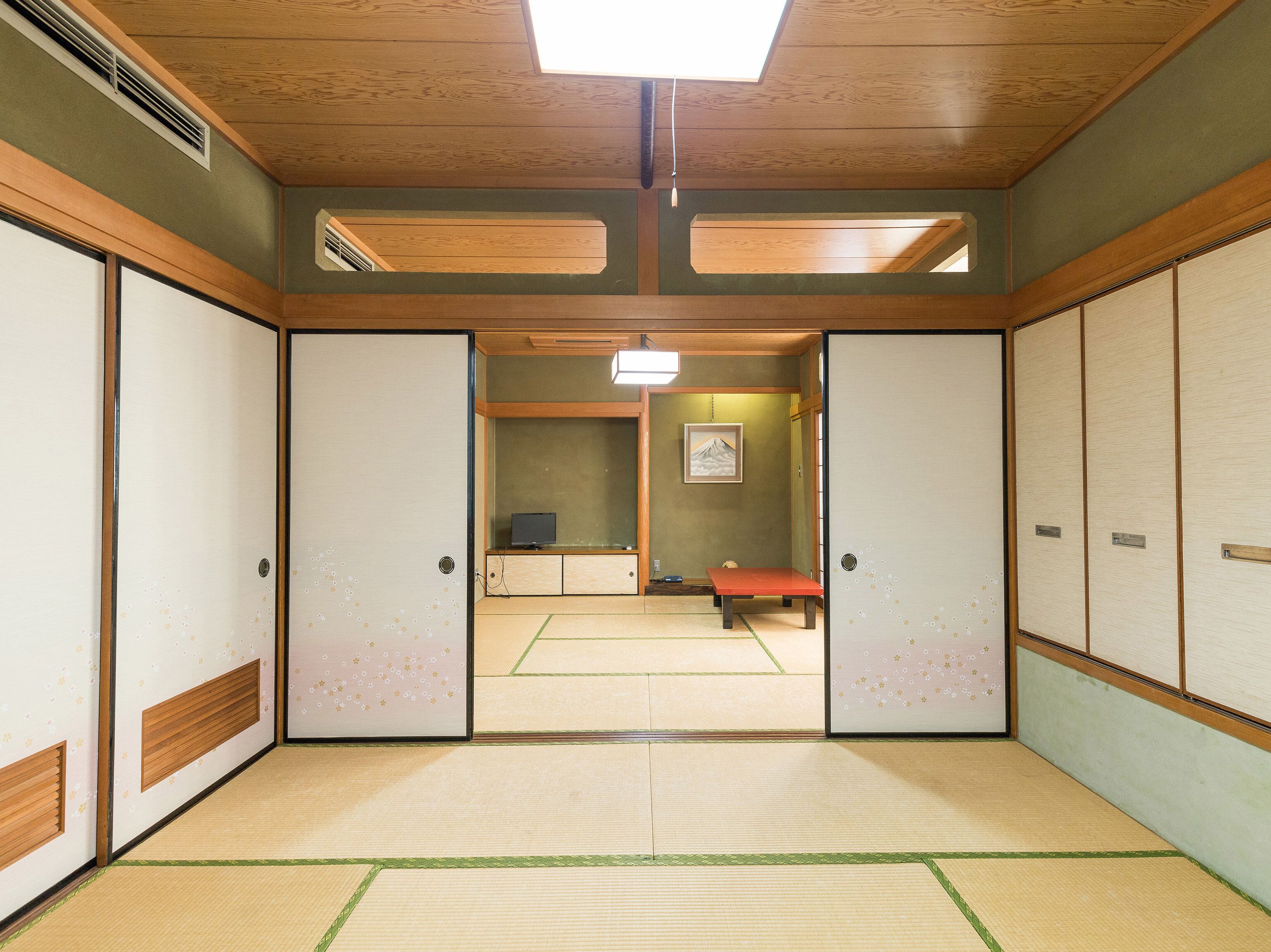 A traditional Japanese room with tatami flooring, sliding doors, and a small table with a red cushion.