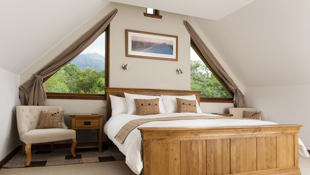 Un dormitorio con una cama de madera, una mesita de noche, una silla y vistas a la montaña a través de la ventana.