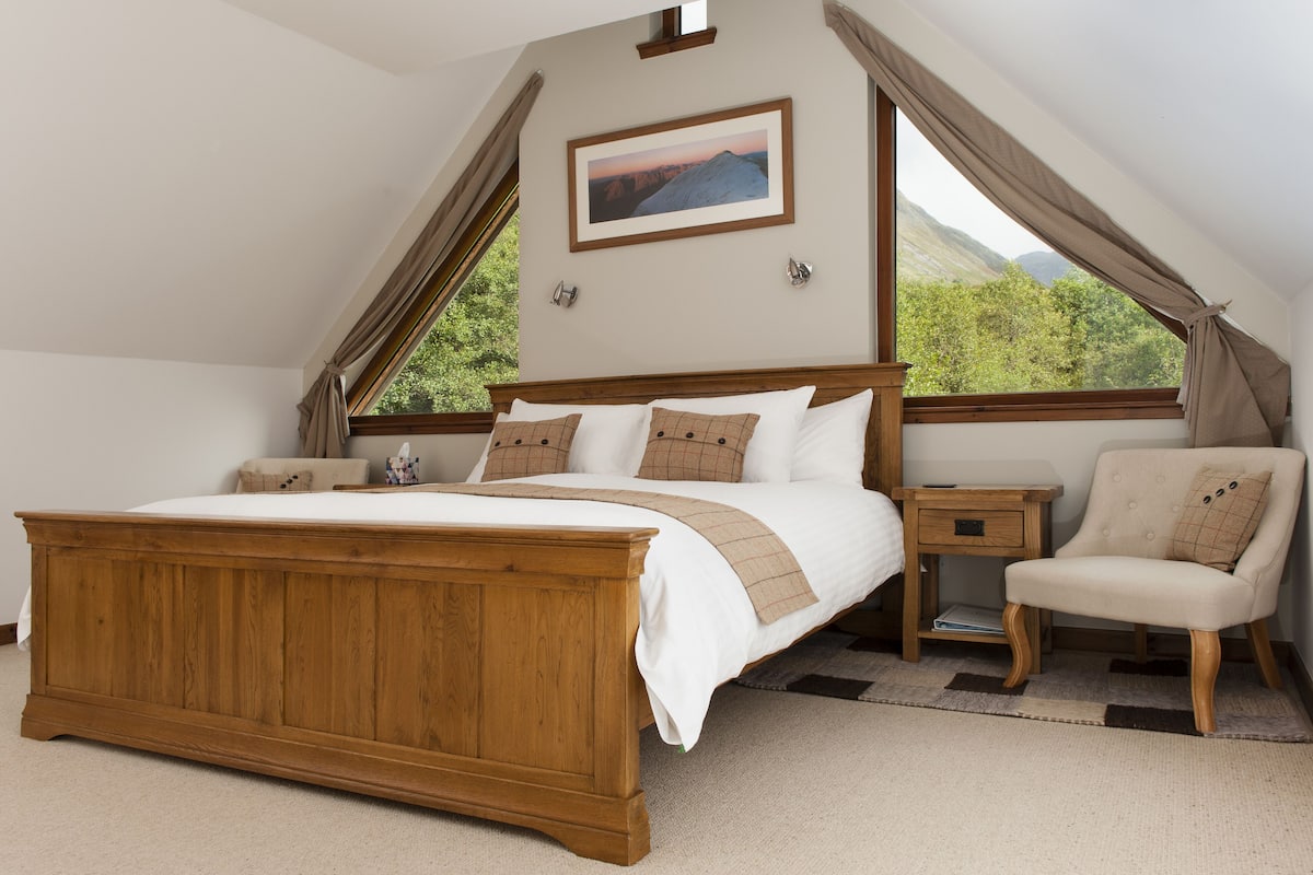 A bedroom with a wooden bed, a nightstand, a chair, and a window with curtains.
