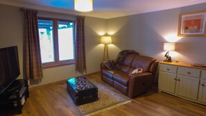 A living room with a leather sofa, a small table with a lamp, a cabinet, and a television. - Strath Lodge Glencoe (Ballachulish)