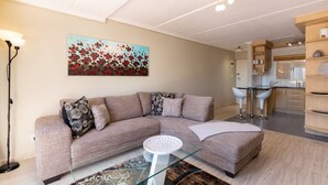 Een moderne woonkamer met een hoekbank, een glazen salontafel en een schilderij aan de muur.