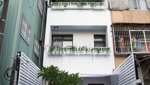 A two-story building with a white facade, a green gate, and a small garden area.