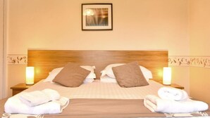 A neatly made bed with pillows, two bedside lamps, and folded towels on the bed.