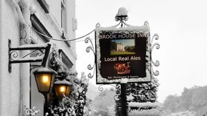 A snow-covered outdoor seating area with a sign for Brook House Inn advertising local real ales, bar, restaurant, and rooms.