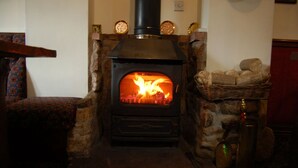 A wood-burning stove with a fire burning inside, set in a stone fireplace with a wooden mantel.