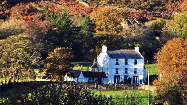 A white building with a traditional design, surrounded by a rural landscape with autumn foliage.