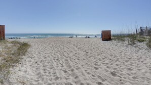 A sandy beach with wooden structures, clear skies, and a calm sea.