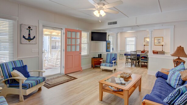 A spacious living room with a ceiling fan, a dining area with a table and chairs, and a large window with blinds.