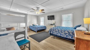 A modern bedroom with two beds, a ceiling fan, a TV, and a desk with a lamp.