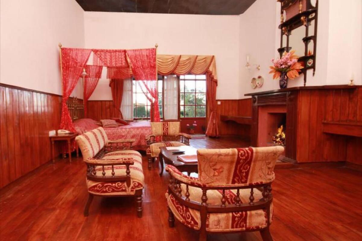 A traditional room with a bed, a fireplace, and a dining area with chairs and a table.