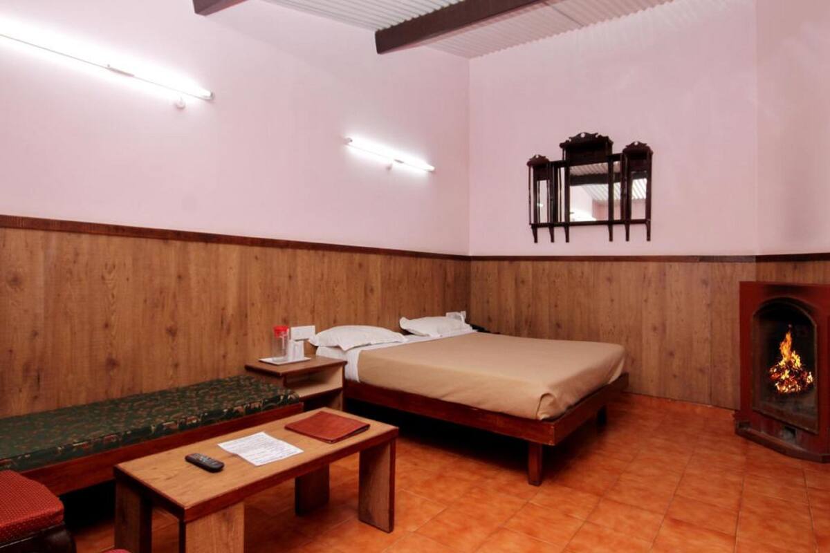 A room with a bed, a wooden desk, a small table, a mirror, and a fireplace.