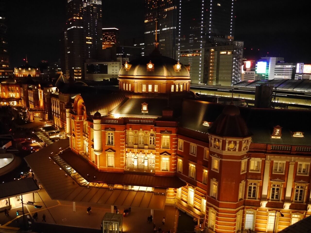 A historic building with a central dome and multiple wings, surrounded by modern skyscrapers.