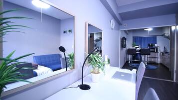 Uma sala de estar moderna com um sofá azul, uma escrivaninha com um laptop, um espelho grande e um vaso de planta.