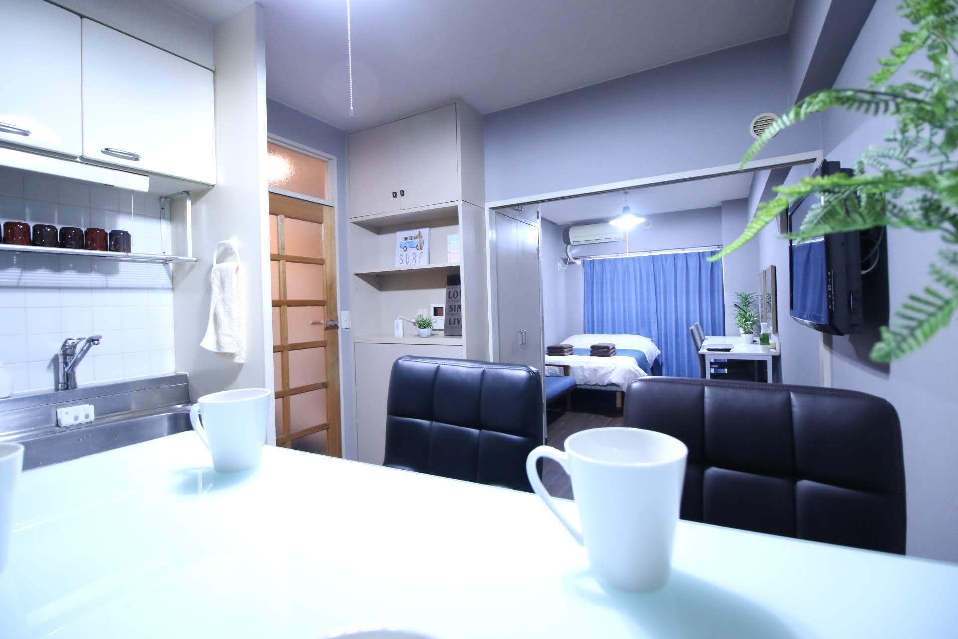 Quarto de hotel compacto com cozinha compacta, área de refeições com mesa e cadeiras, cama e televisão fixada na parede.