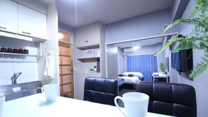 A compact hotel room with a kitchenette, a dining area with a table and chairs, a bed, and a TV mounted on the wall.
