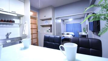 Quarto de hotel compacto com cozinha compacta, área de refeições com mesa e cadeiras, cama e televisão fixada na parede.
