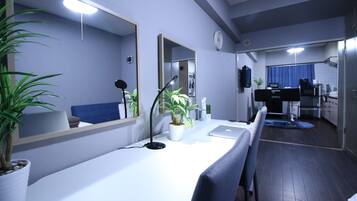 Uma sala de estar moderna com um sofá branco, um espelho grande, uma escrivaninha com um laptop e uma planta em vaso.